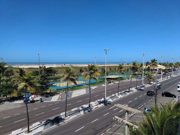 A coastal road with a beach in the background, palm trees, and a sports court.