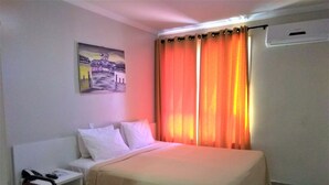 A hotel room with a bed, white pillows, a bedside table with a phone, and a painting on the wall. - Simas Praia Hotel (Aracaju)
