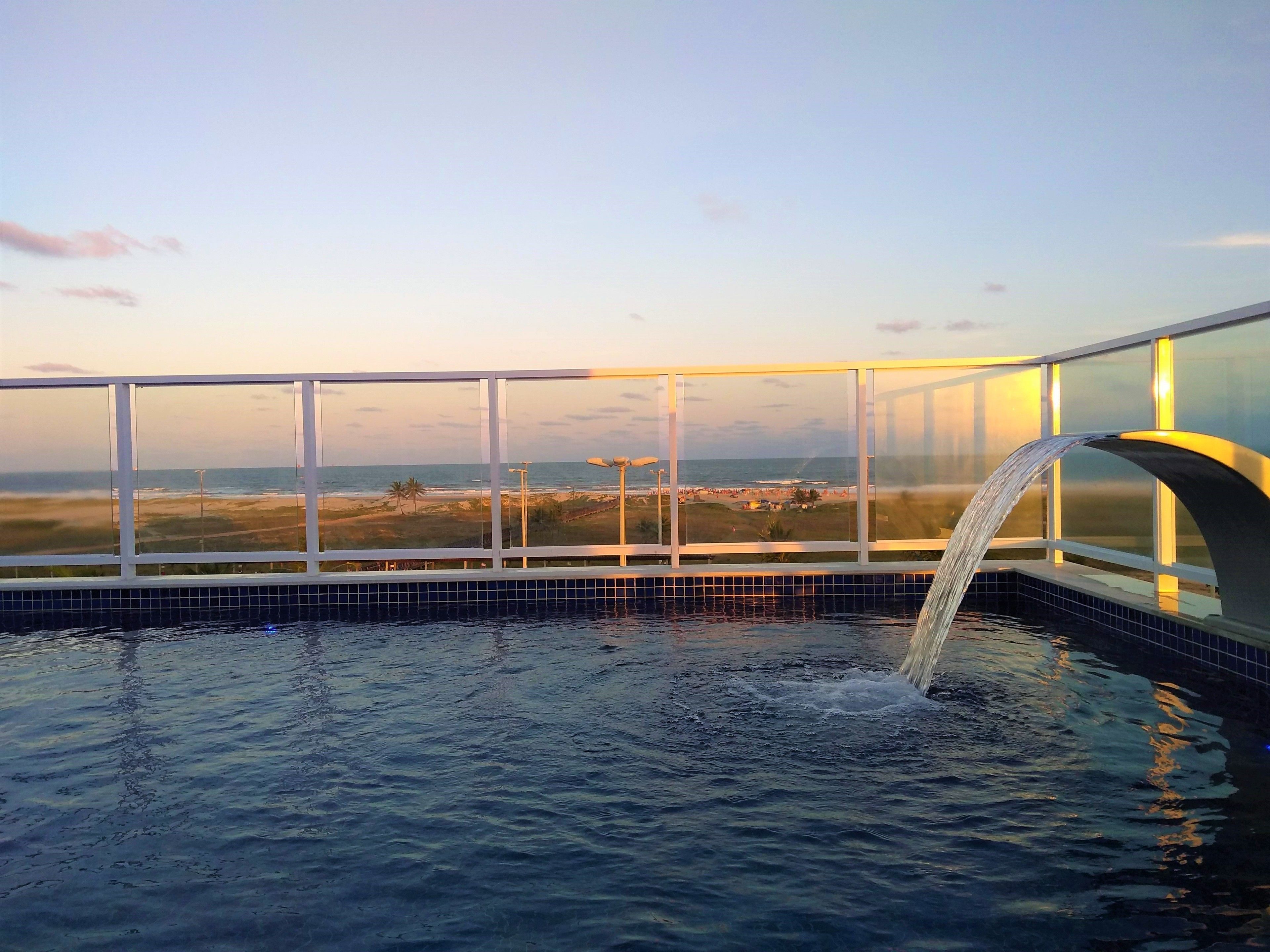 A pool with a waterfall feature and a view of the beach and ocean through large windows.