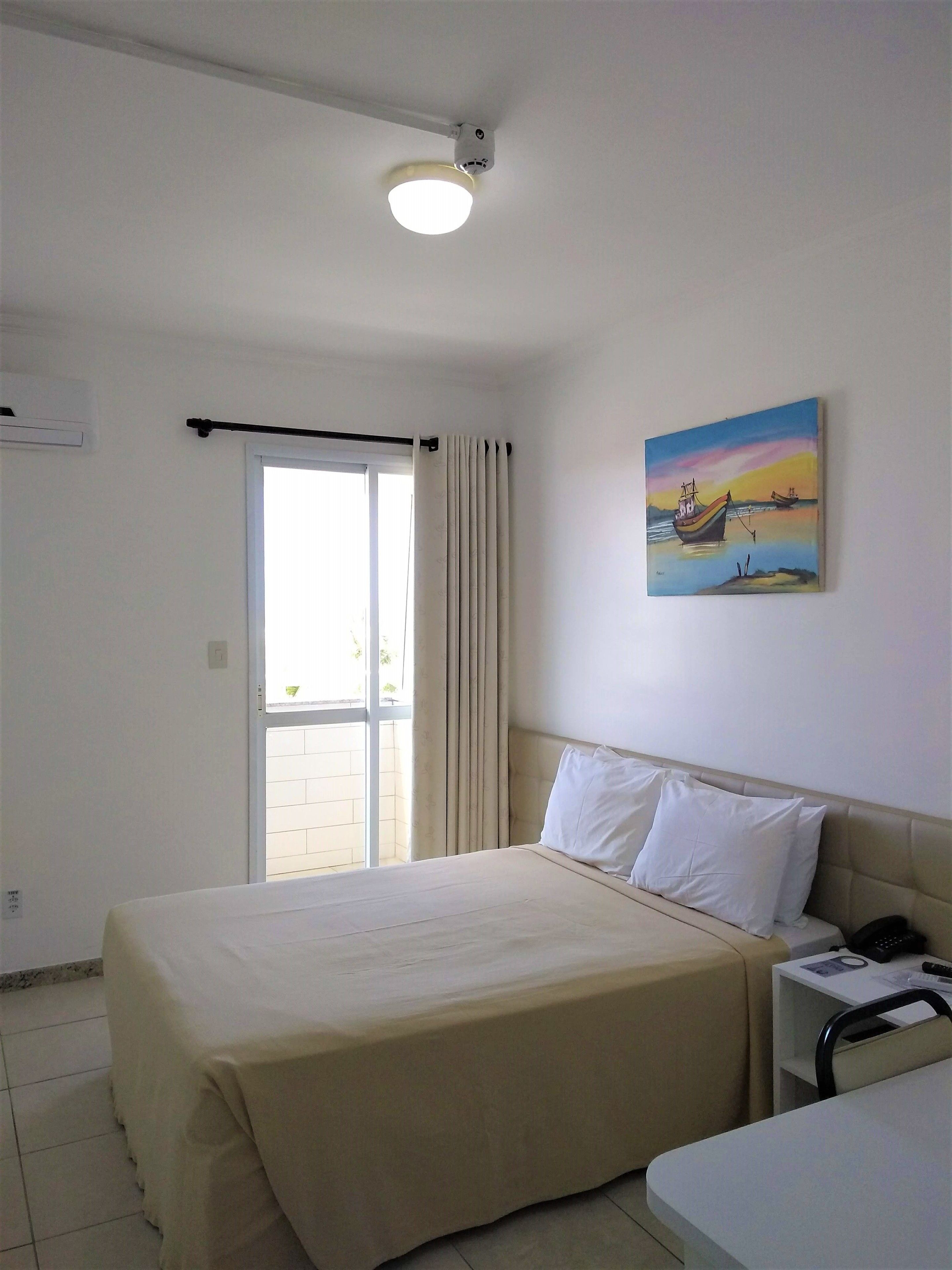 Habitación de hotel con cama, mesita de noche con teléfono y un cuadro de barcos en la pared.