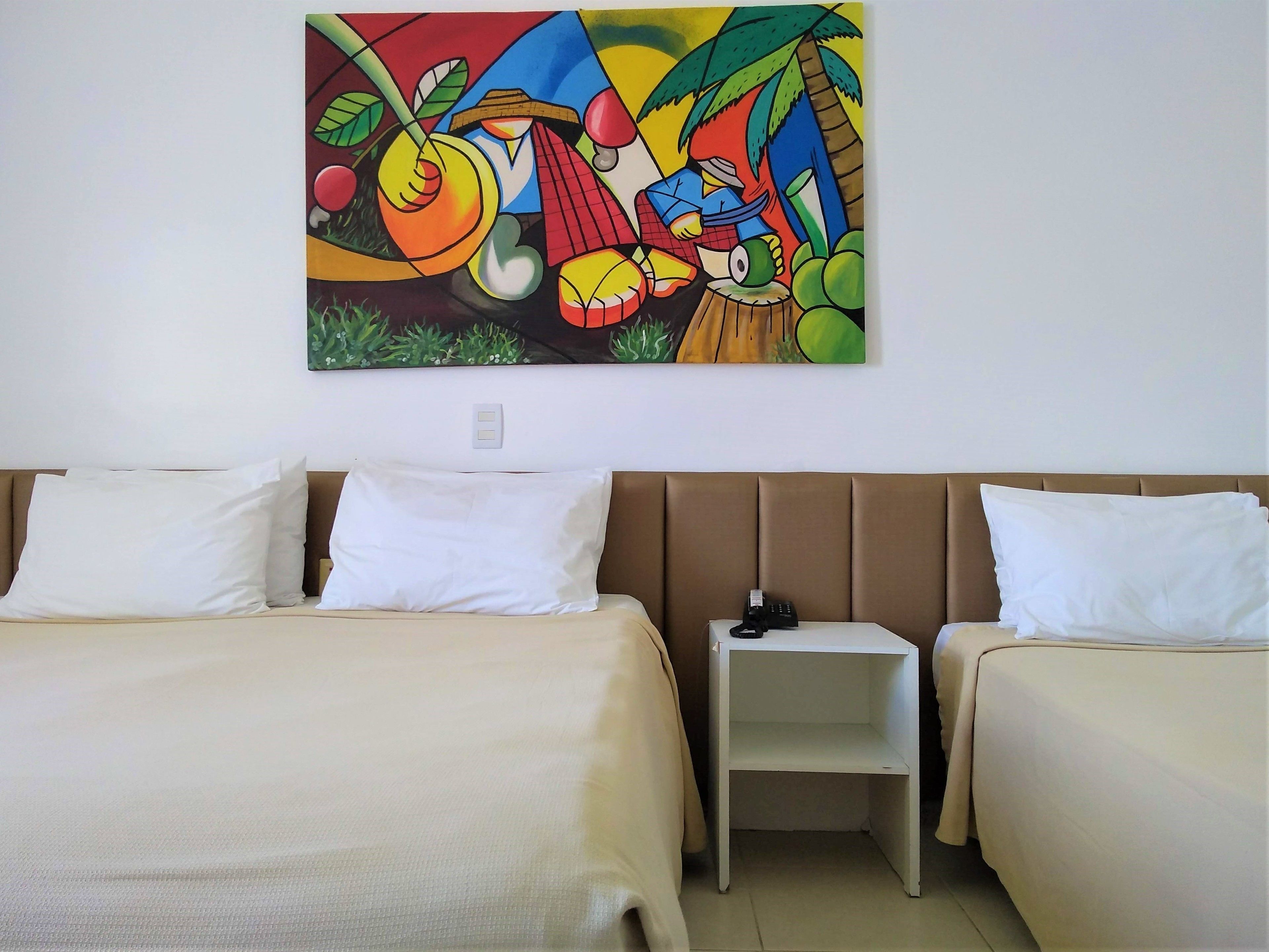A hotel room with two beds, a small bedside table with a phone, and a colorful abstract painting on the wall.