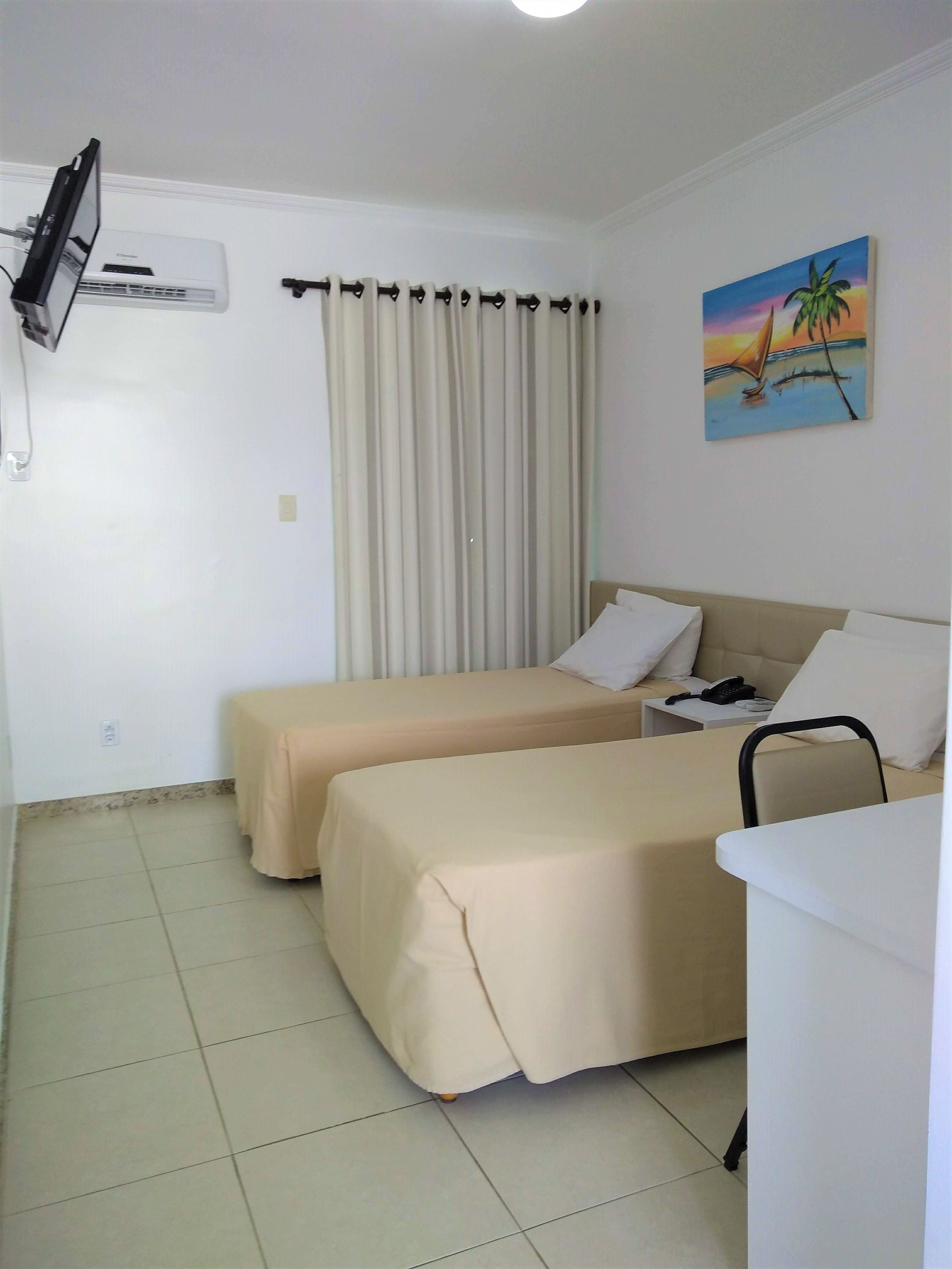 Habitación de hotel con dos camas, un televisor montado en la pared, un cuadro de un atardecer y una ventana con cortinas.