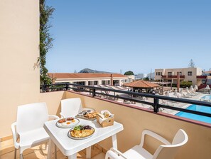 A balcony with a table set for breakfast, overlooking a pool and buildings. - Kambos Village (Chania)