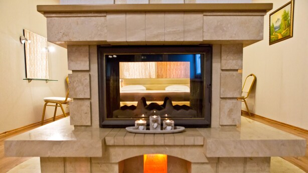 A modern fireplace with a bed visible through the glass, a small table with candles, and a framed picture on the wall. - Hotel Olsi (Chisinau)