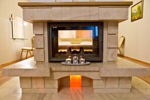 A modern fireplace with a bed visible through the glass, a small table with candles, and a framed picture on the wall. - Hotel Olsi (Chisinau)