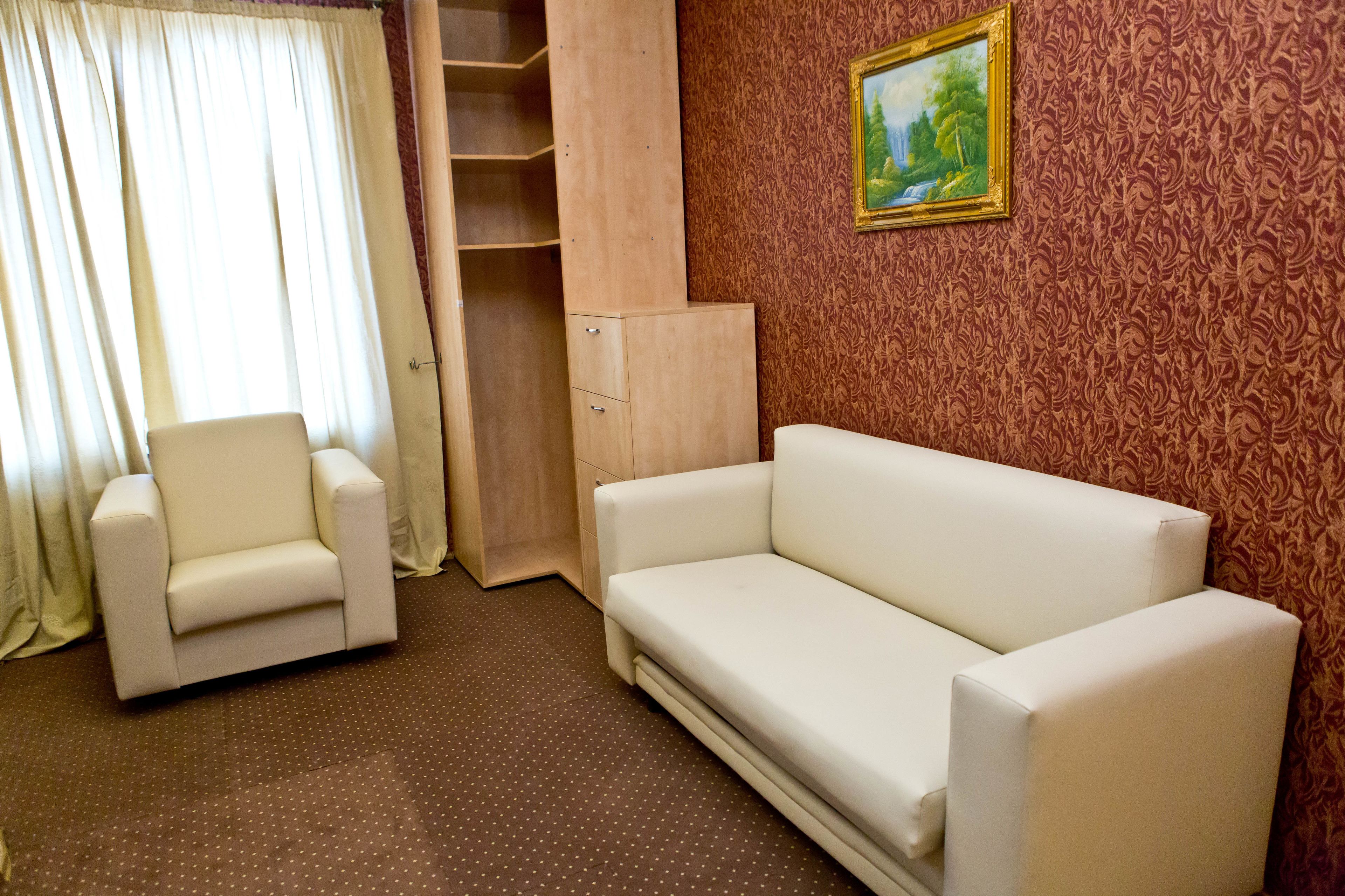 Une pièce avec un fauteuil blanc, un canapé blanc, un meuble en bois et un papier peint à motifs.