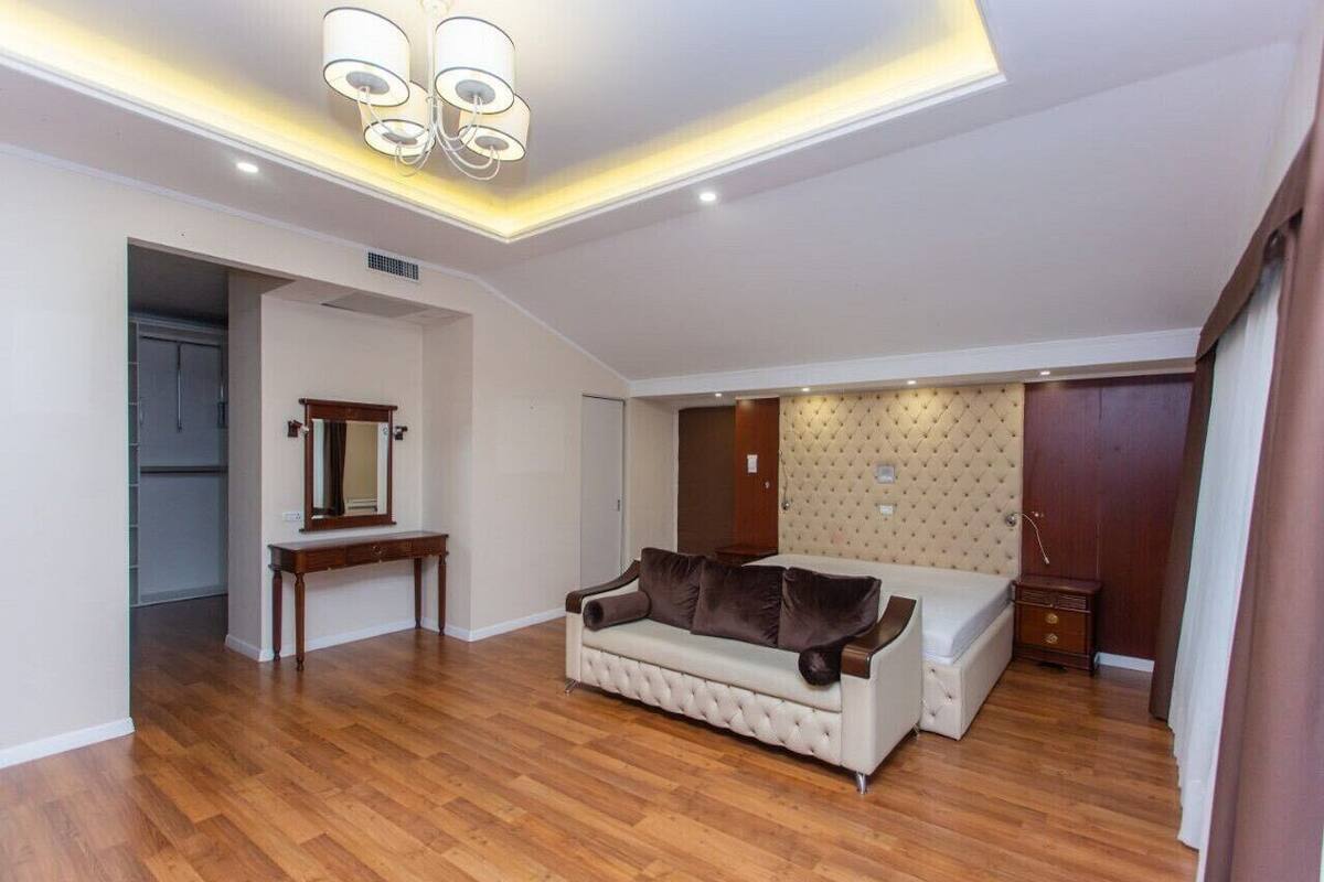 A spacious room with a wooden floor, a white sofa, a wooden cabinet, and a mirror.