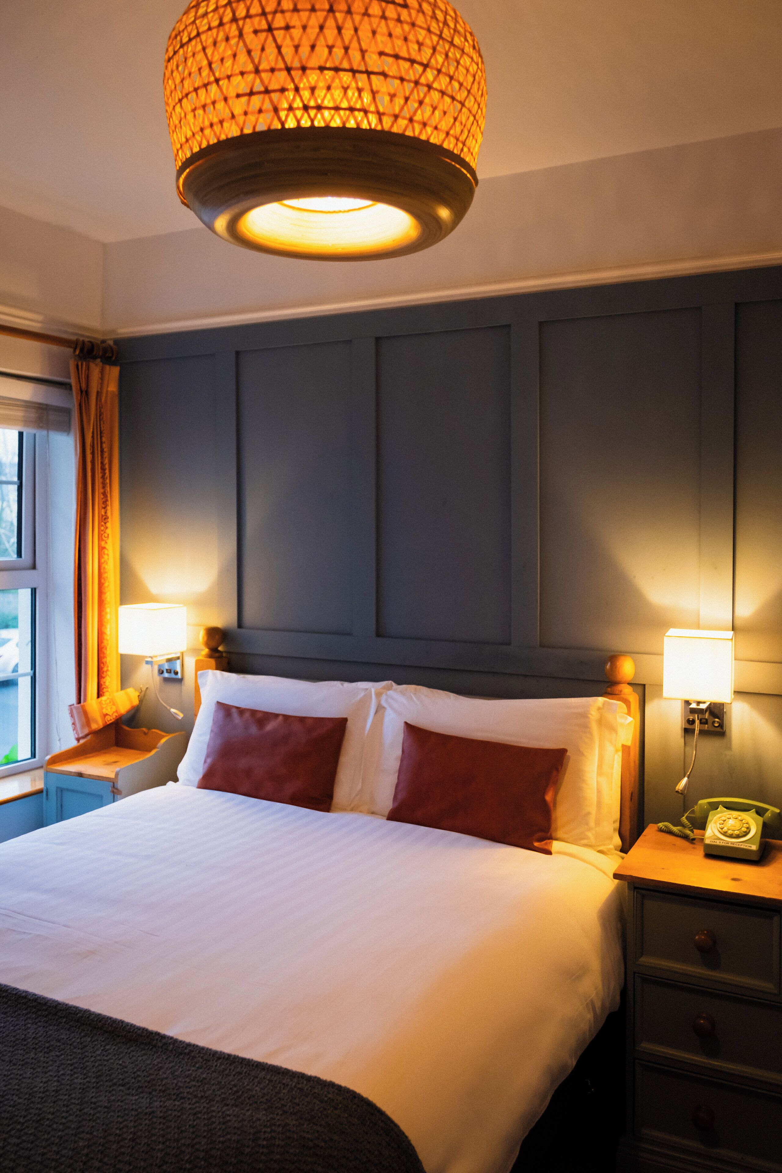 A hotel room with a large bed, two bedside tables with lamps, a telephone, and a window with curtains.