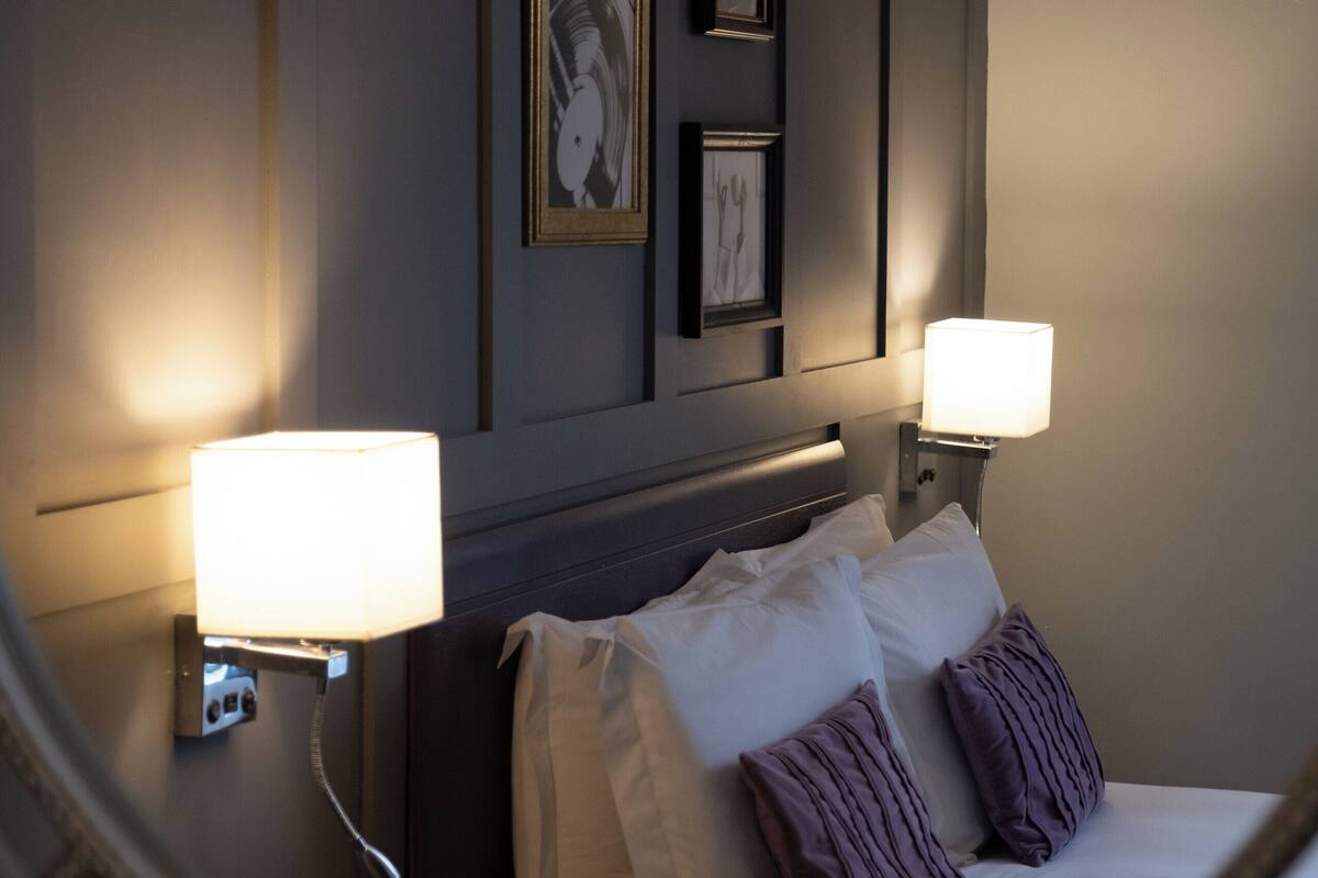 Una habitación de hotel con una cama, dos lámparas de pared y obras de arte enmarcadas.