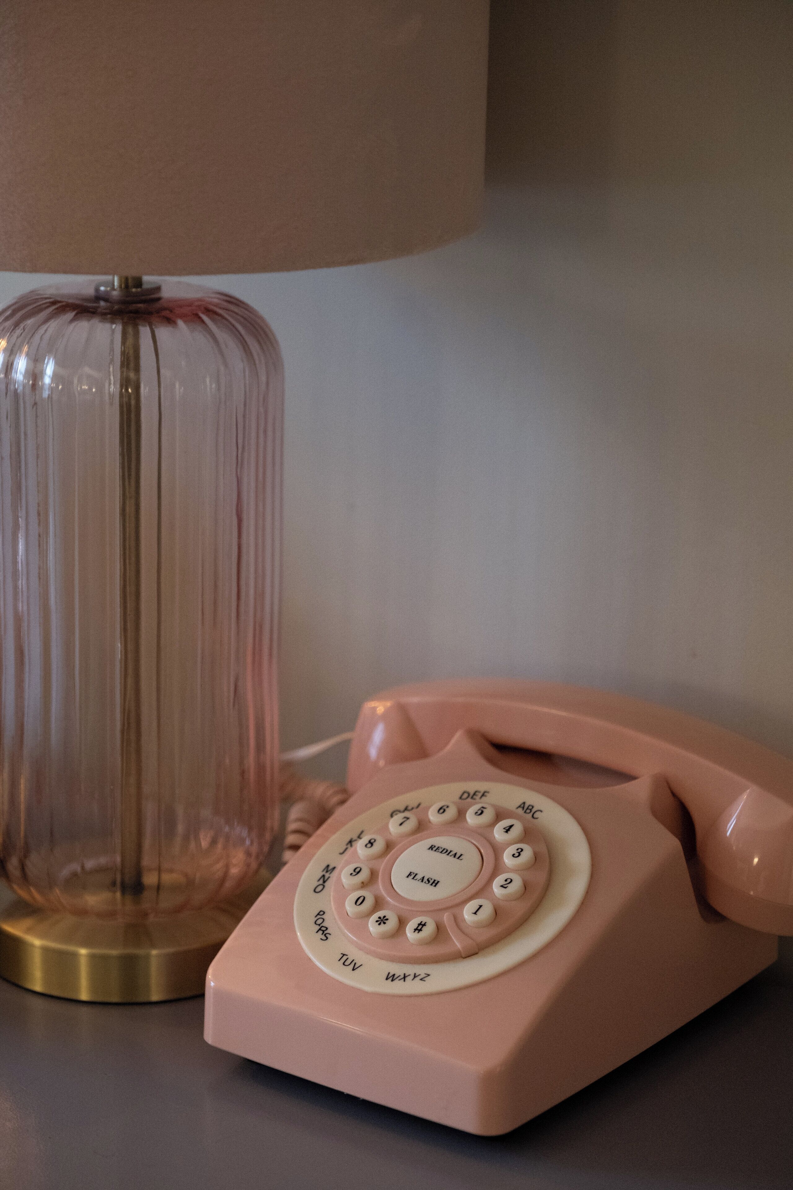 Un telefono con tastierino a quadrante rosa accanto a una lampada in vetro trasparente.