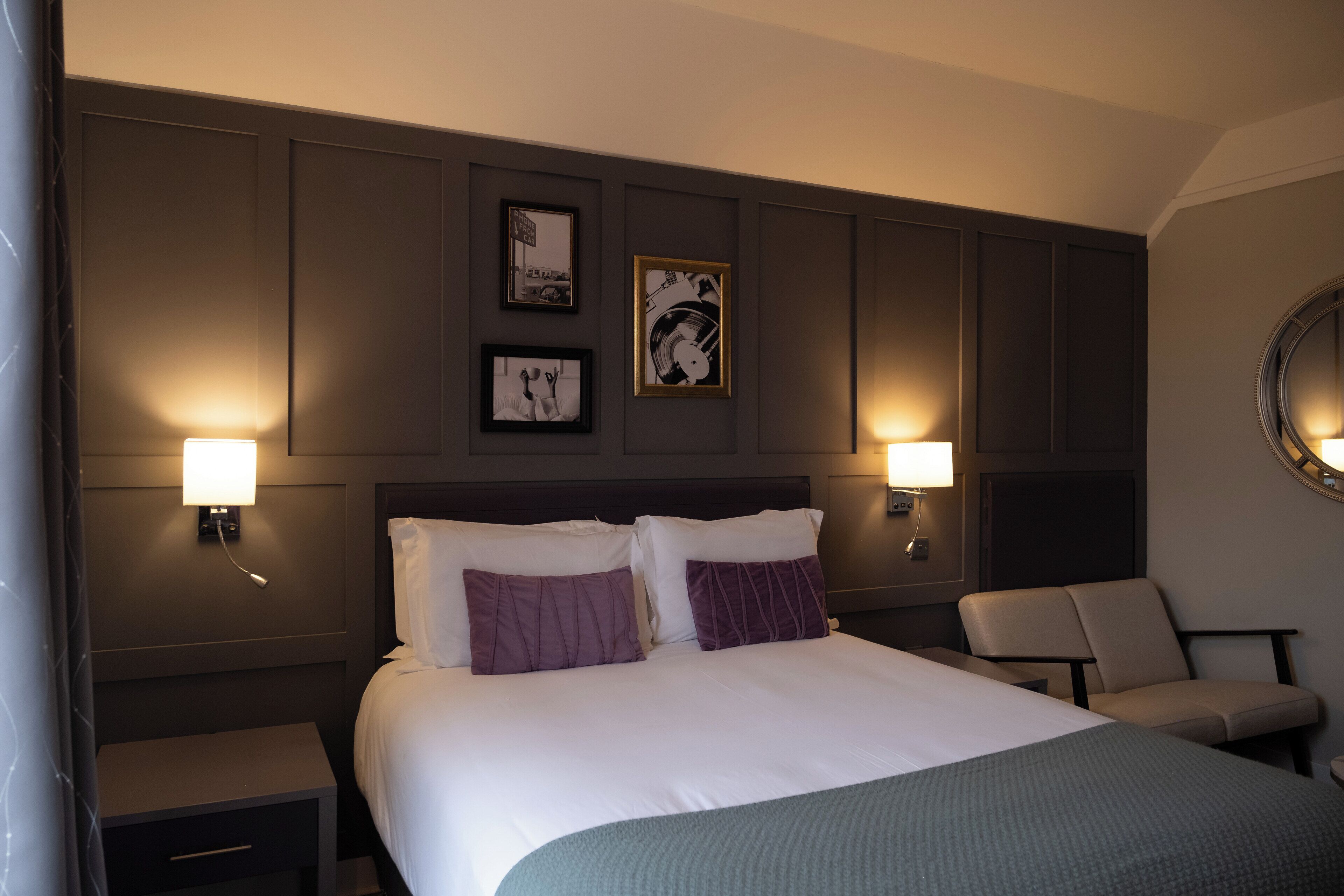 A hotel room with a large bed, two bedside tables, a chair, and wall-mounted lamps.