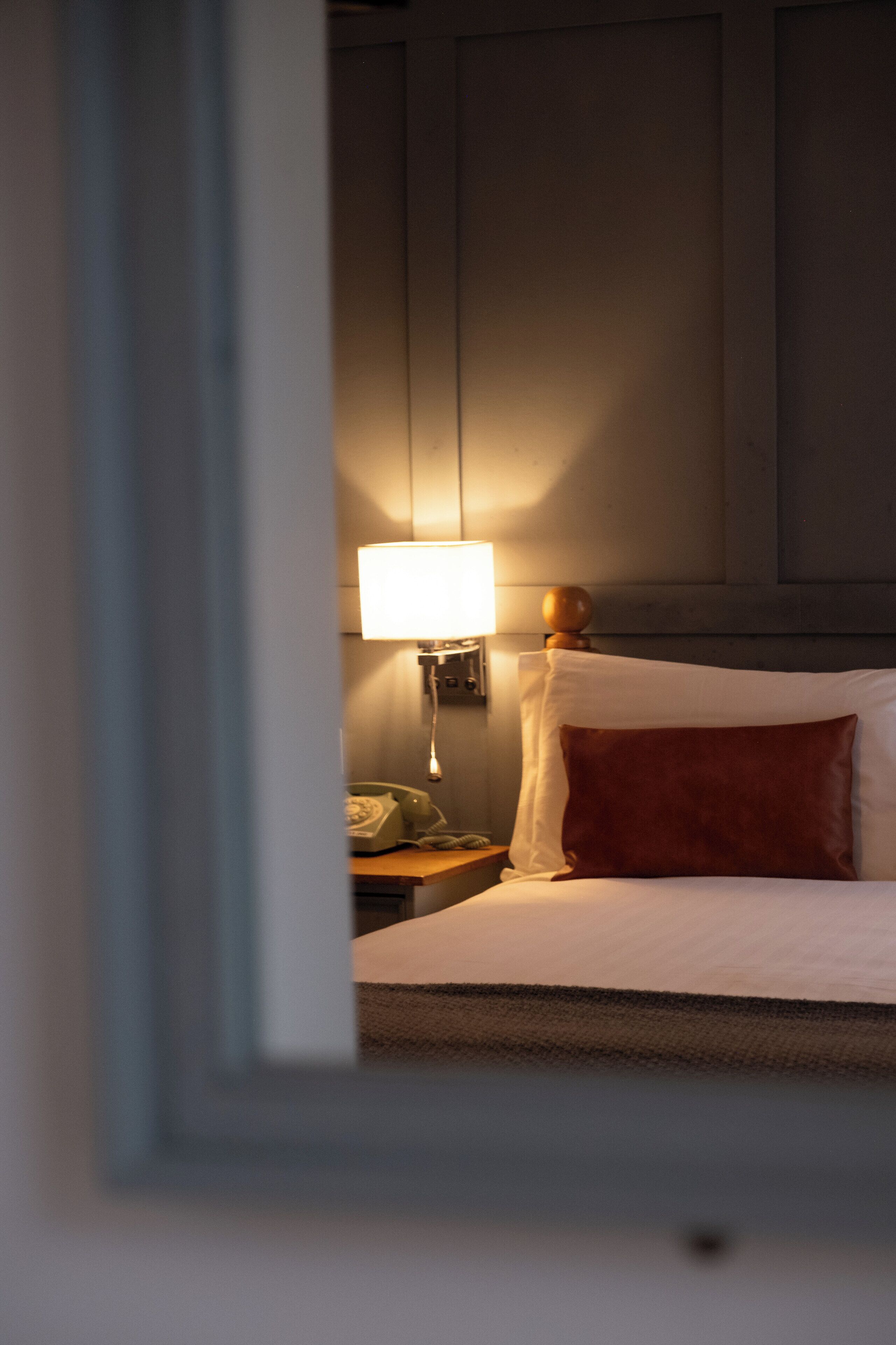 Una habitación de hotel con cama, mesita de noche, lámpara y teléfono.