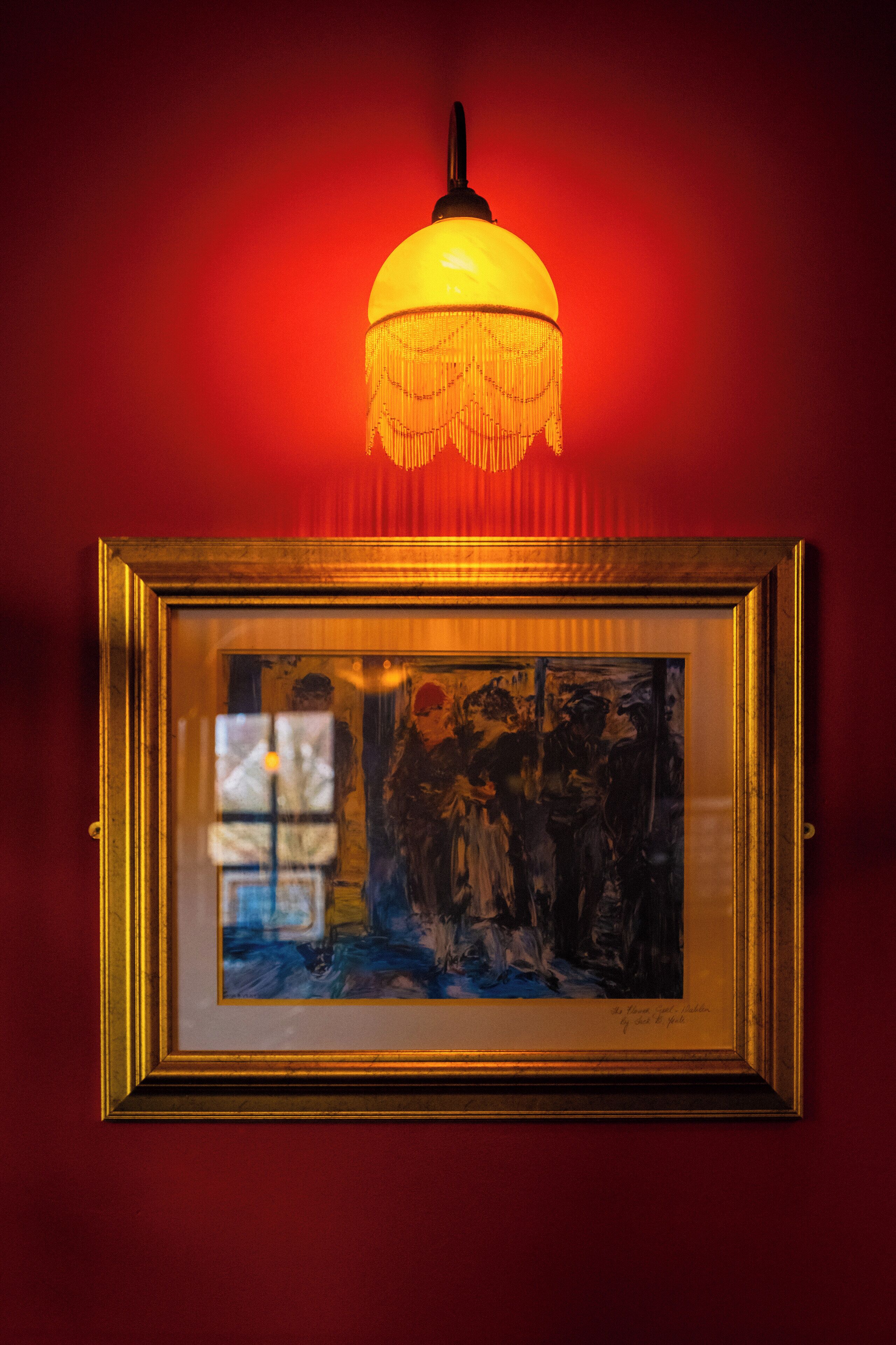 Una obra de arte enmarco iluminada por un lámpara colgante.