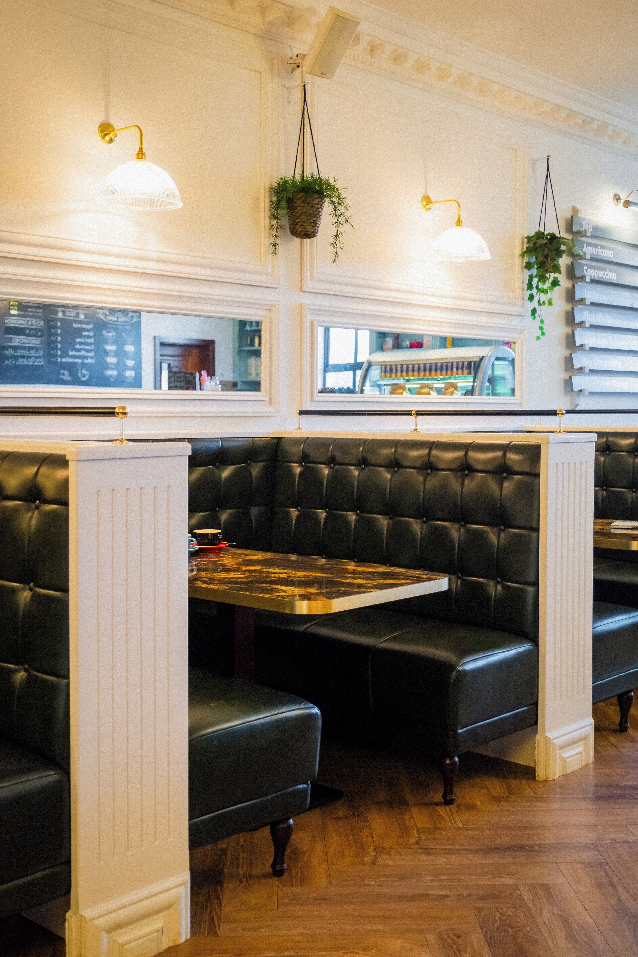 A restaurant interior with black leather booths, white paneling, hanging plants, and a menu board.