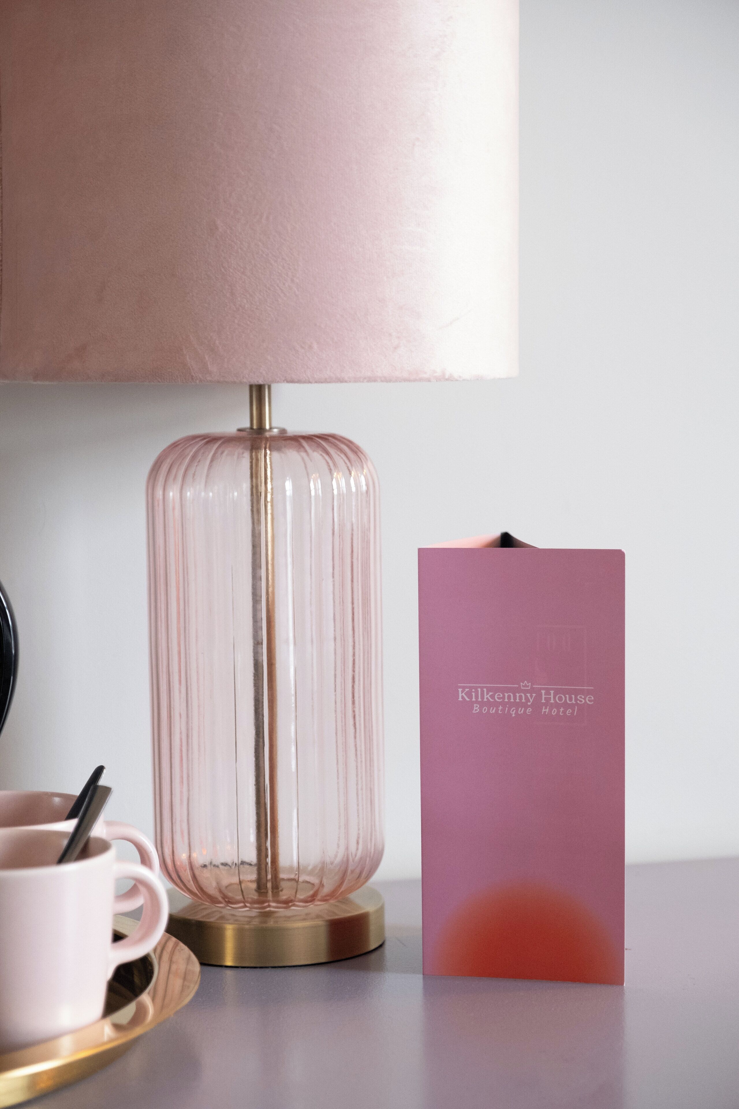 A pink lamp, a pink mug, and a pink brochure on a table.