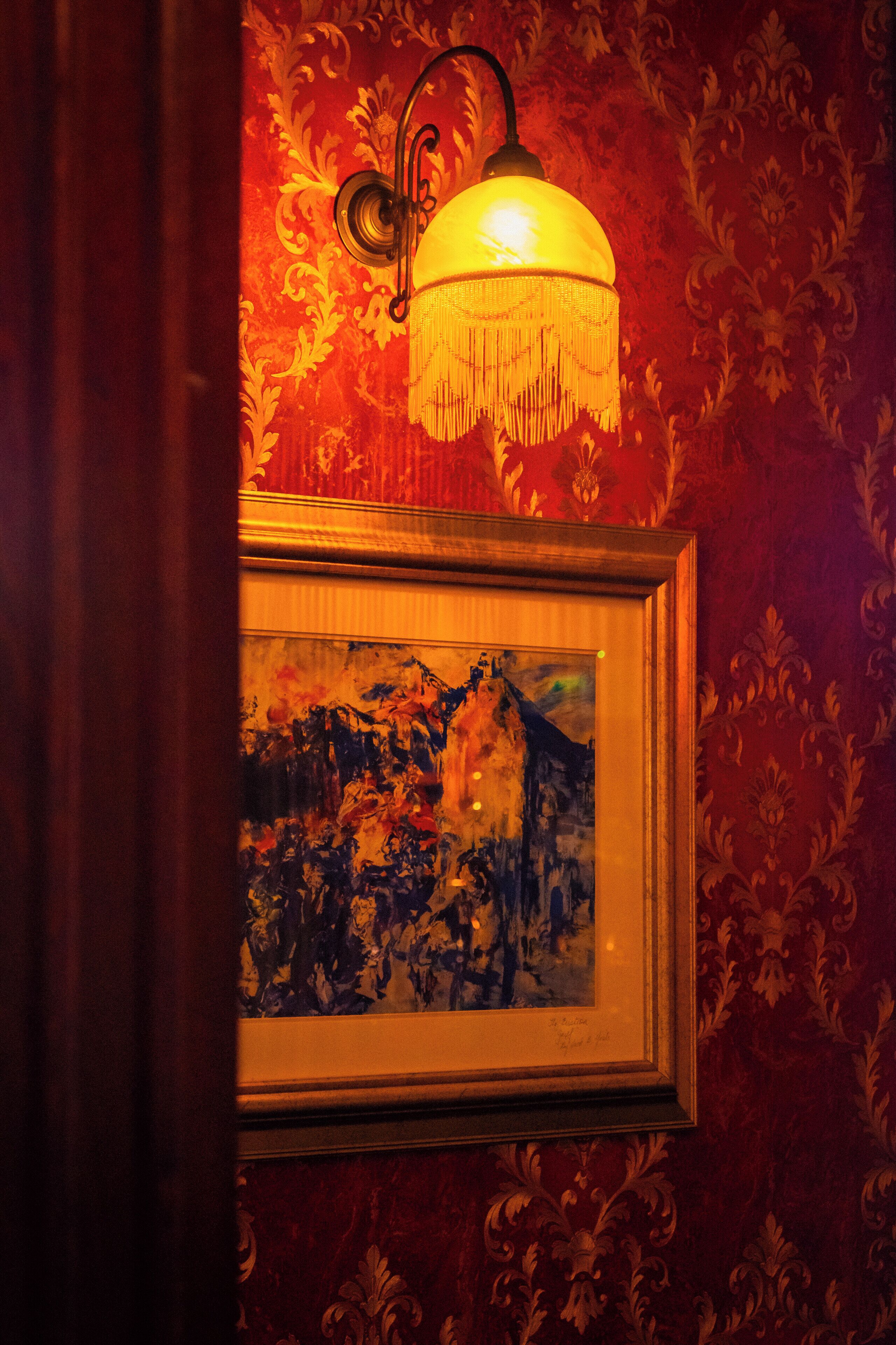 Un tableau encadré représentant un paysage, accroché à un mur recouvert d’un papier peint décoratif.