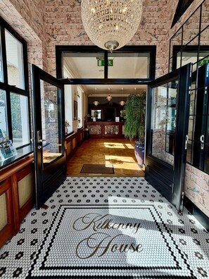 Un hall d’hôtel avec un sol à motifs, un grand lustre et un comptoir d’accueil.