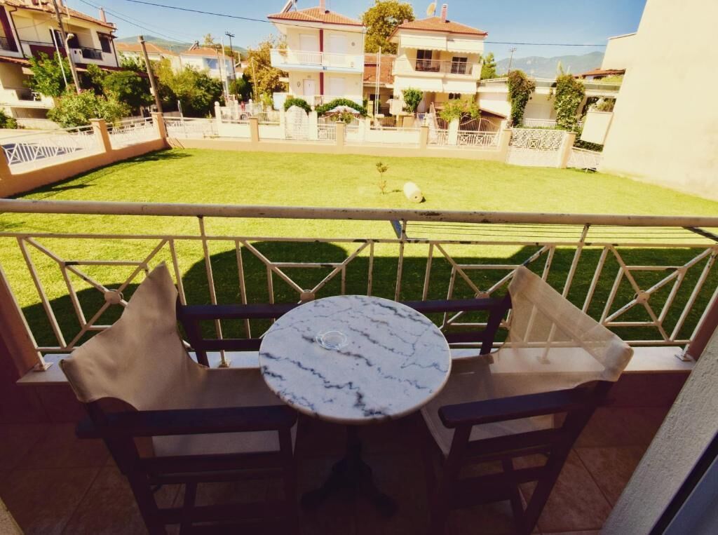 Un balcón con mesa y sillas, con vista a un césped cuidado y casas vecinas.