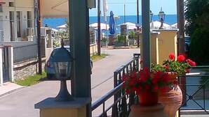 A seaside balcony with large terracotta pots of red flowers, a metal railing, and a view of the sea and buildings in the background. - Pfaffenhofen (Volvi)