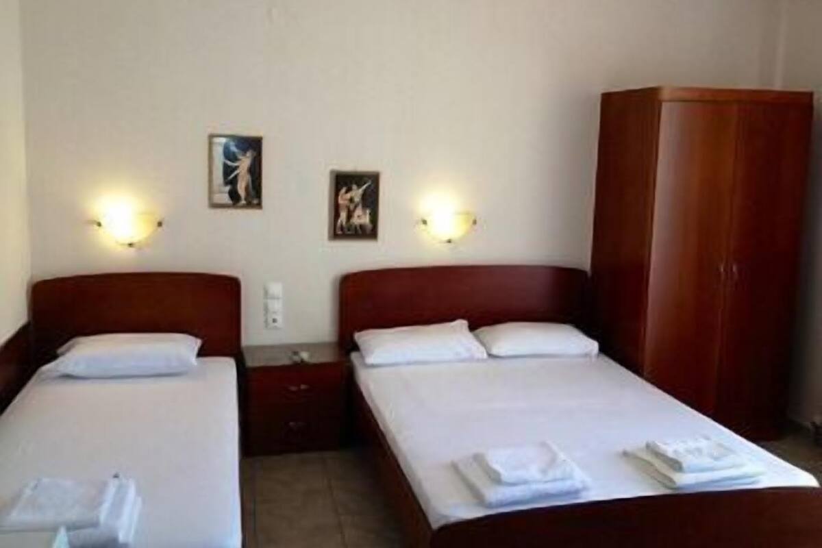 A hotel room with two beds, each with white linens and pillows, and a wooden wardrobe.