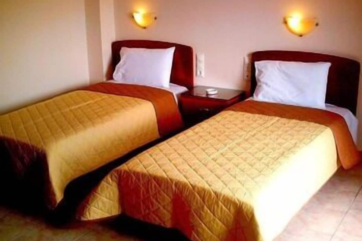 A hotel room with two single beds, each with a quilted bedspread and white pillows. There are two bedside tables with lamps.