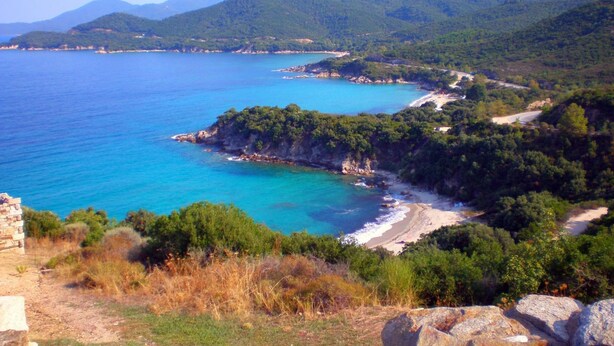 A coastal landscape with a clear view of the sea, a sandy beach, and lush green hills in the background. - Pfaffenhofen (Volvi)