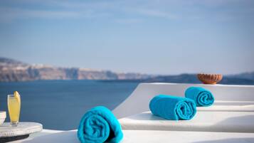 A seaside view with a table set with a glass of drink and two rolled towels.