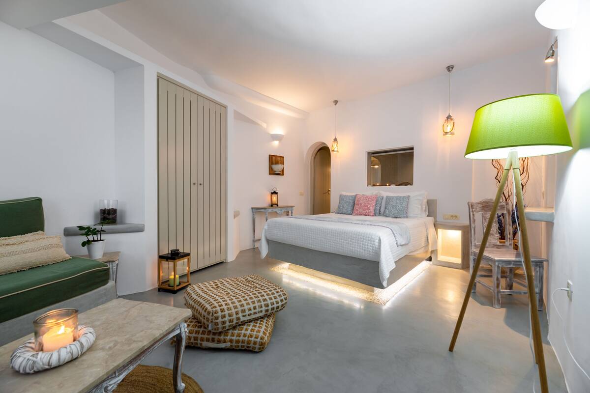 A modern bedroom with a bed, bedside tables, a green sofa, a floor lamp, and a small table with a candle.