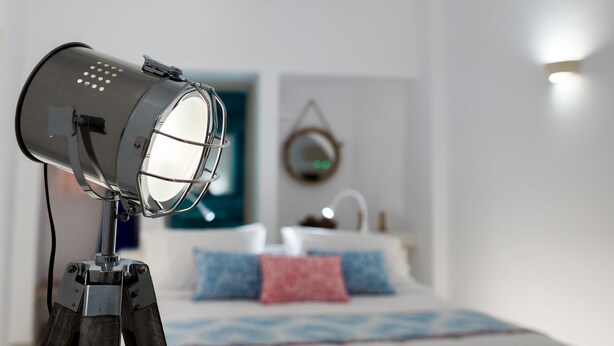 Quarto com cama, espelho na parede e luminária sobre tripé.