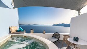 Un jacuzzi con vistas al mar, una mesa, sillas y dos faroles en un balcón.