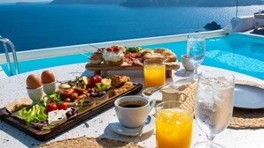 Uma mesa de café da manhã com diversos alimentos, bebidas e vista para o mar.