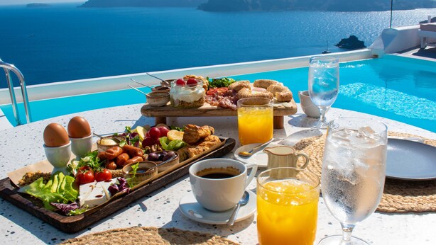 Una mesa de desayuno con diversos alimentos, bebidas y vista al mar.
