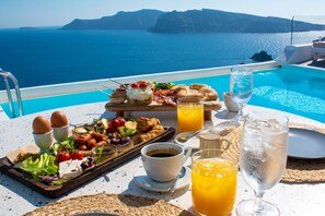 A breakfast table with a variety of foods, drinks, and a view of the sea. - Kima Oia Suites (Santorini)