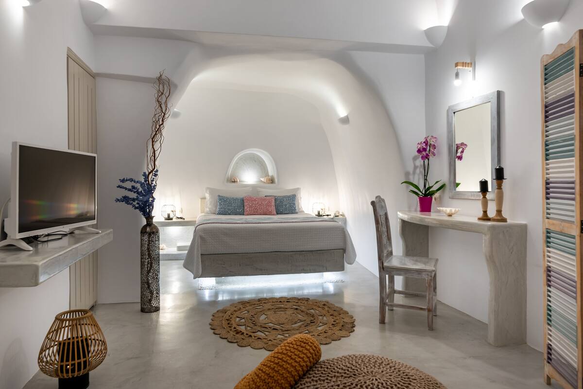 A modern bedroom with a sloped ceiling, a bed with a white headboard, a bedside table, a chair, a television, and decorative items.