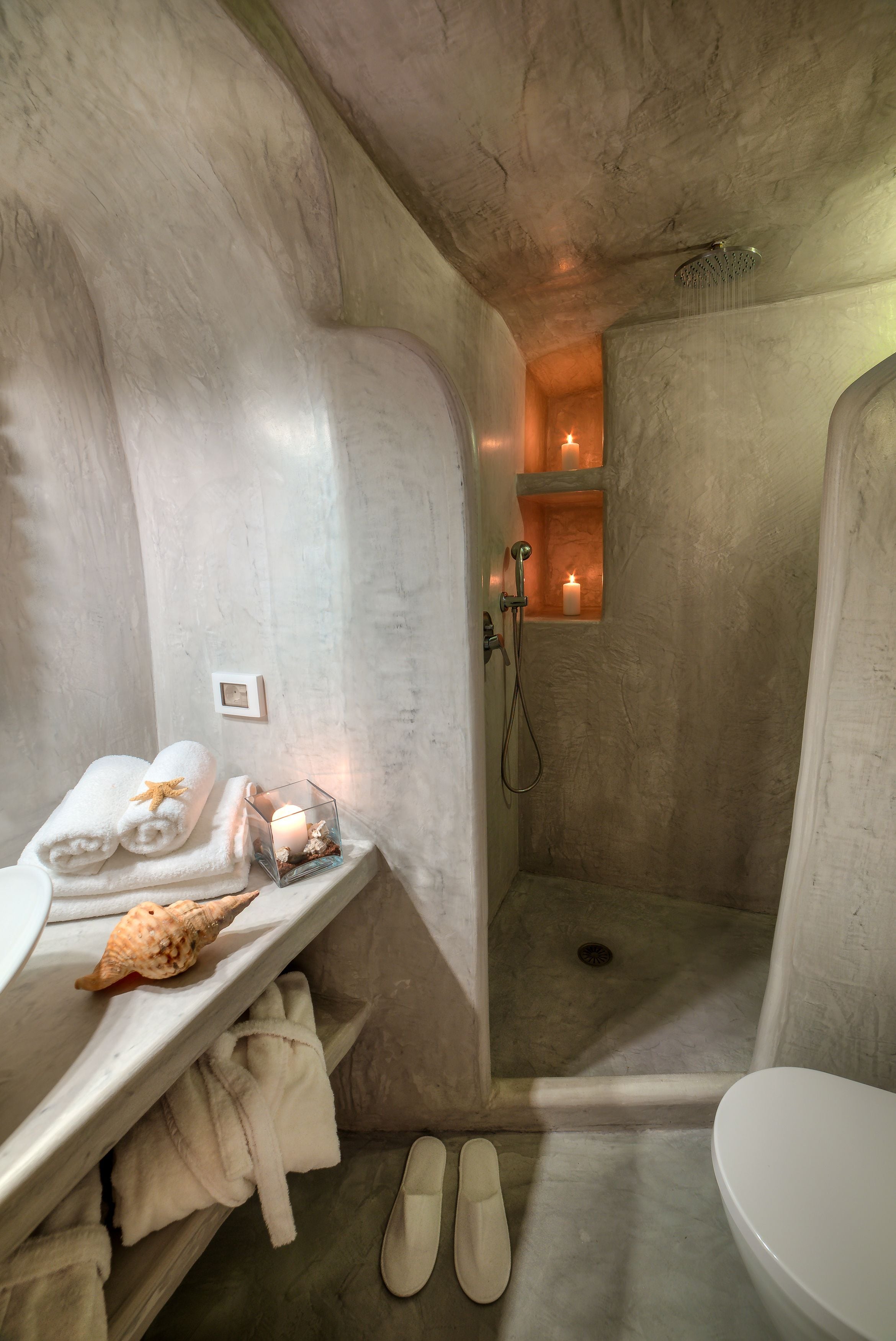 A bathroom with a shower, a toilet, and a vanity with towels and a candle.