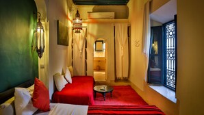 A hotel room with two beds, a small table, and a window with decorative iron bars. - Riad Dar Sara (Marrakech)