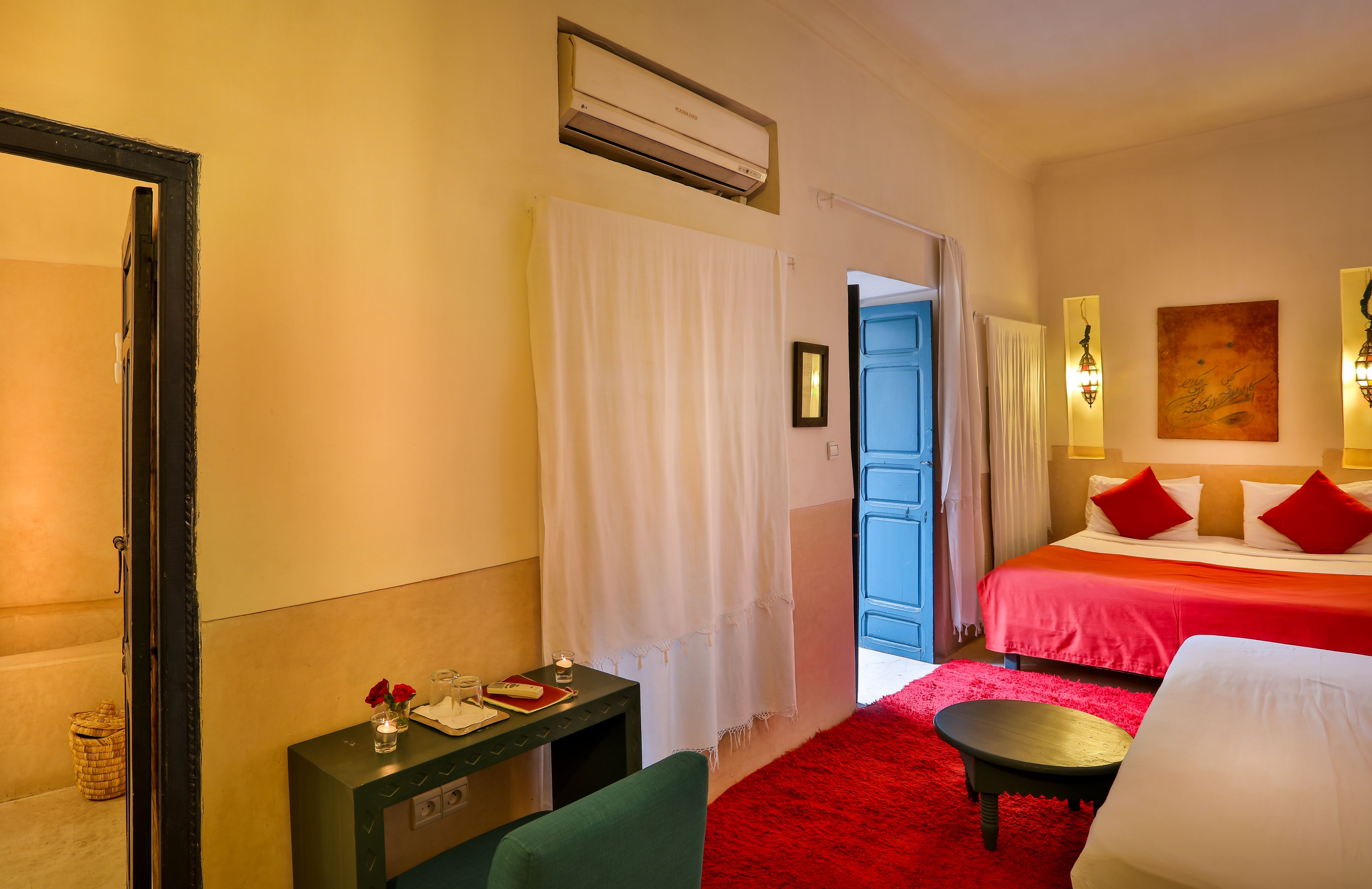 Een hotelkamer met een bed, een bureau met lamp, een stoel, een rood tapijt en een schilderij aan de muur.
