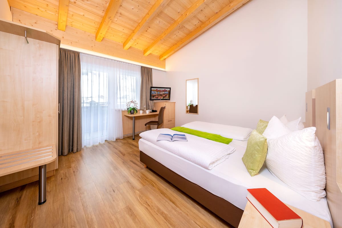 Une chambre d’hôtel moderne avec un plafond en bois, un grand lit avec une literie blanche, un bureau avec une chaise et une armoire.