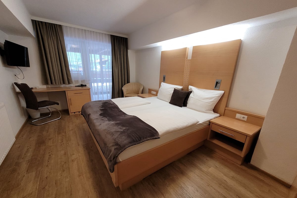 Une chambre d’hôtel avec un grand lit, un bureau, une chaise, une télévision et une fenêtre avec des rideaux.