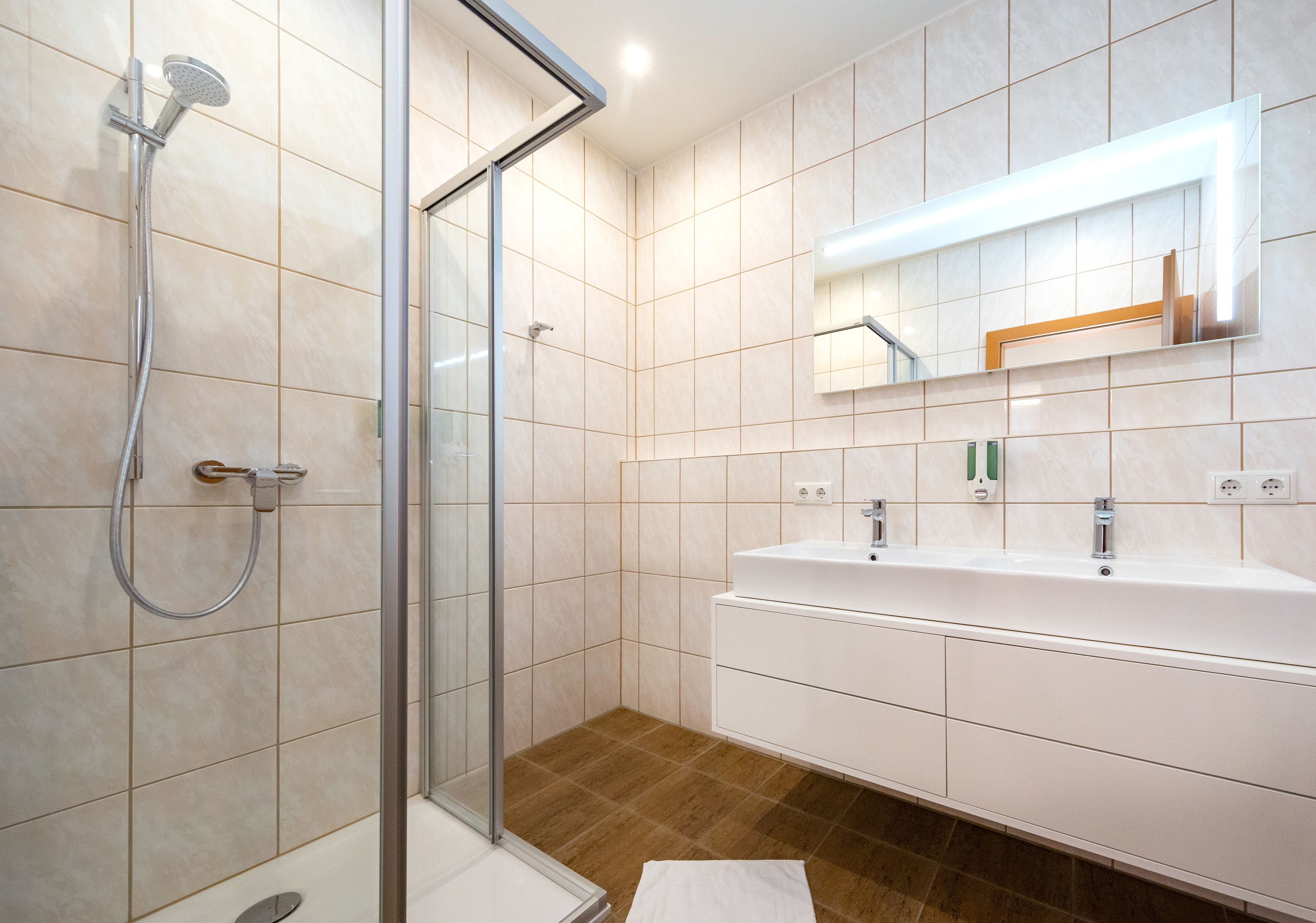 Un baño moderno con cabina de ducha de vidrio, un lavabo blanco y un espejo con iluminación integrada.
