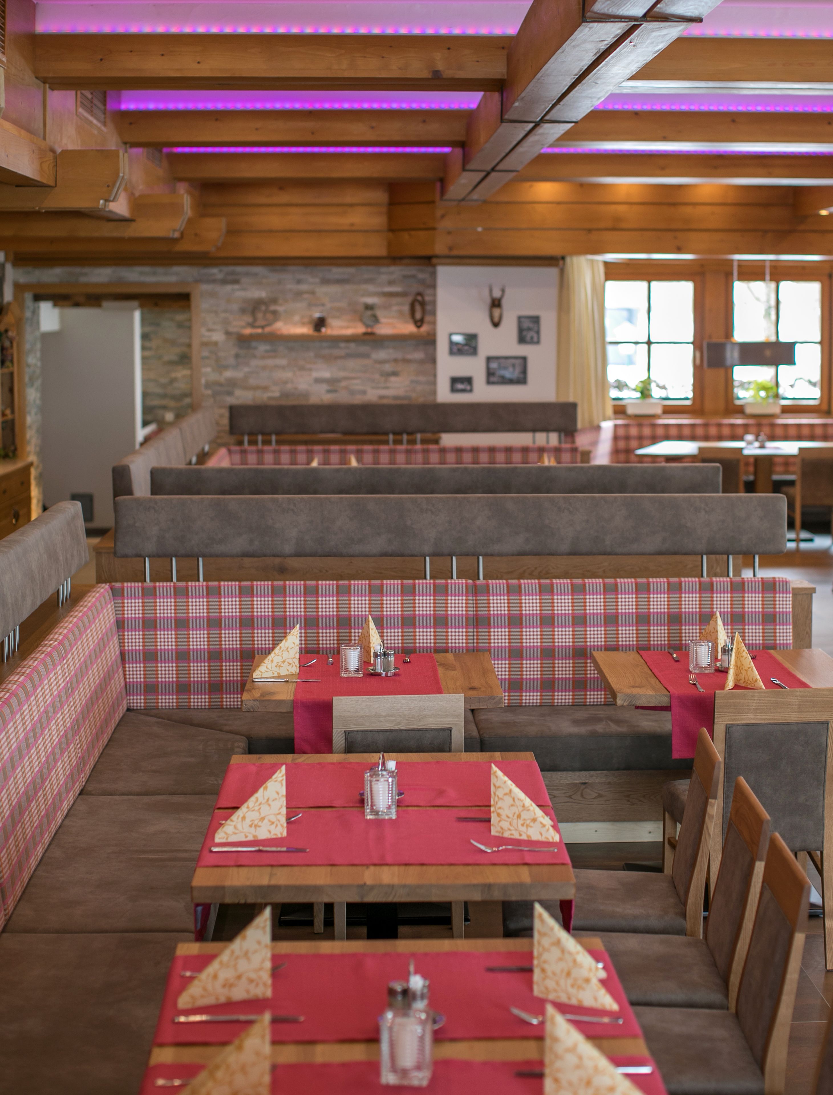 A restaurant with wooden booths and tables, red tablecloths, and a stone wall with framed pictures.