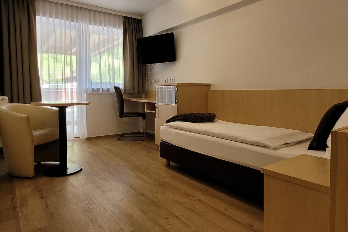 Une chambre d’hôtel avec un lit, un bureau, une chaise, une télévision et une fenêtre avec des rideaux.