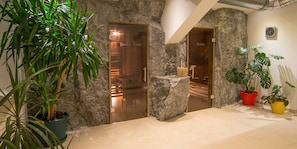 Entrada de un spa con paredes de piedra, una puerta de madera y plantas en macetas.