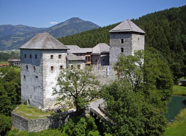 Un castillo de piedra histórico con múltiples torres, rodeado de abundante vegetación y un río.