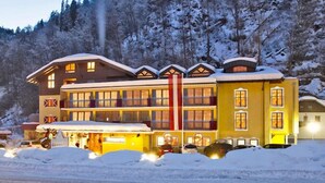 A multi-story hotel with a ski lift in the background, surrounded by snow-covered trees. - Hotel Badhaus (Zell am See)