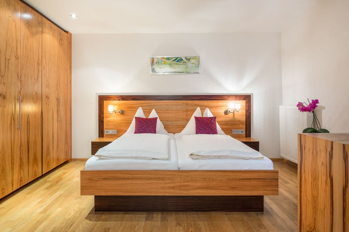 A double bed with a wooden headboard, two bedside tables with lamps, a radiator, and a wooden wardrobe.