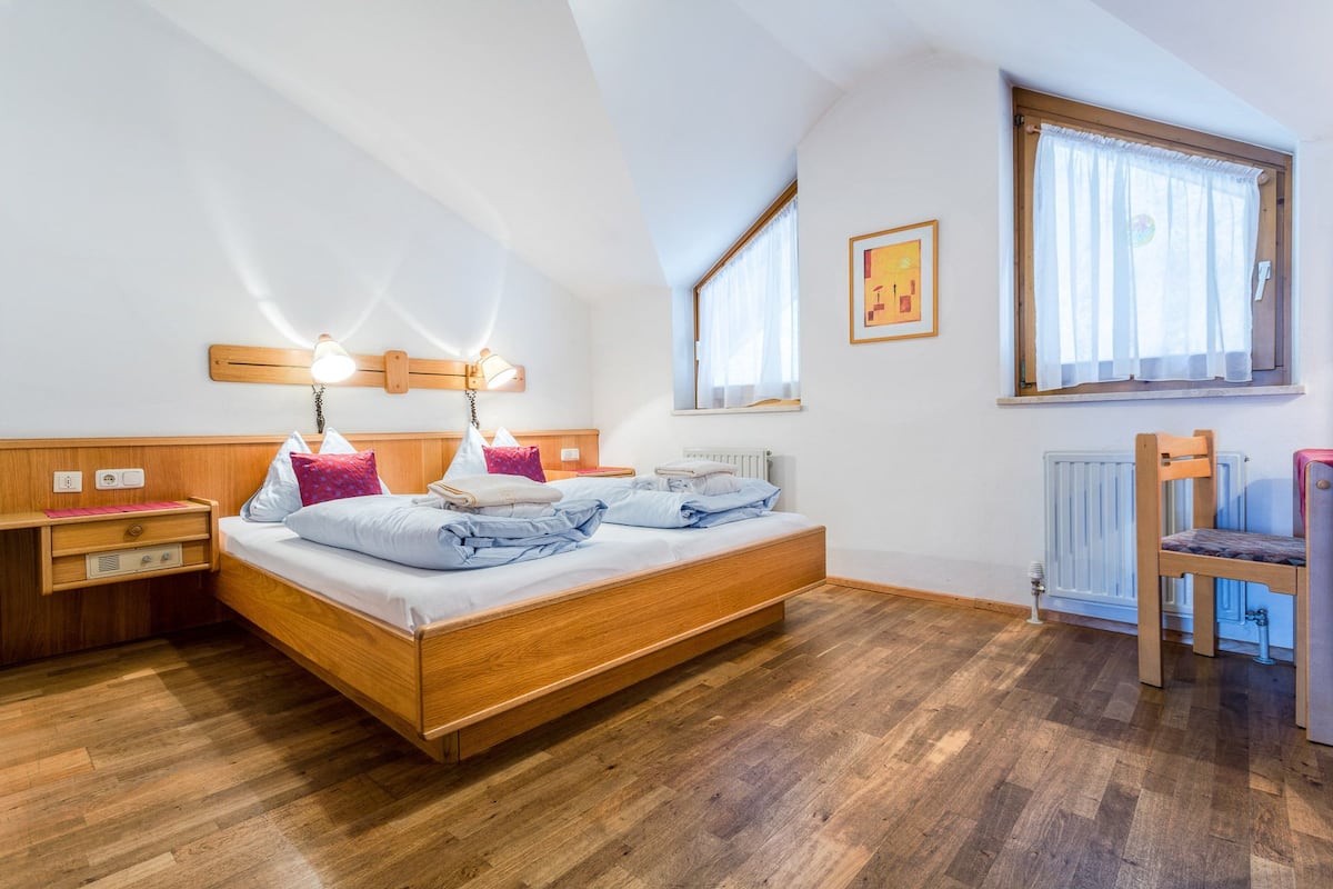 A bedroom with a wooden bed, bedside tables, a chair, and a window with curtains.