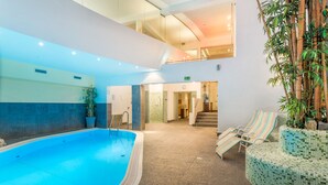 A pool area with a clear blue pool, a staircase leading to an upper level, and lounge chairs with striped cushions. - Hotel Badhaus (Zell am See)