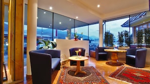 A modern interior with large windows, a seating area with sofas and a round table, and a view of the cityscape. - Hotel Badhaus (Zell am See)
