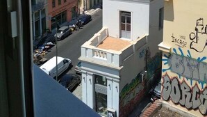 A view of a city street with buildings, a clear sky, and a graffiti-covered wall. - Pella Inn Hostel (Athens)